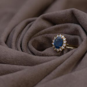 Close-up of a sapphire and diamond gold ring on brown suede, highlighting luxury jewelry details.