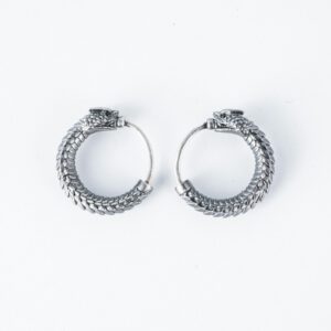 Close-up of intricate silver dragon-themed hoop earrings on a white backdrop.