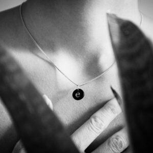Close-up of a necklace with a pendant on bare skin in black and white.